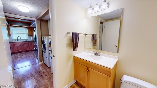 bathroom featuring a textured ceiling, hardwood / wood-style floors, vanity, washing machine and dryer, and toilet