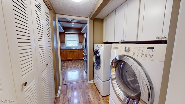 clothes washing area featuring cabinets, a textured ceiling, sink, washer and clothes dryer, and light wood-type flooring