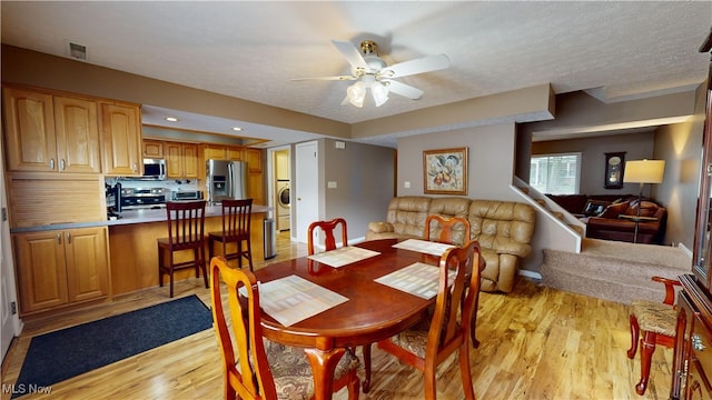 dining area featuring light wood-type flooring, a textured ceiling, ceiling fan, and washer / dryer