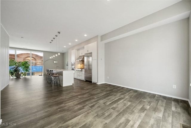 kitchen with a breakfast bar area, dark wood-type flooring, white cabinets, high end fridge, and an island with sink