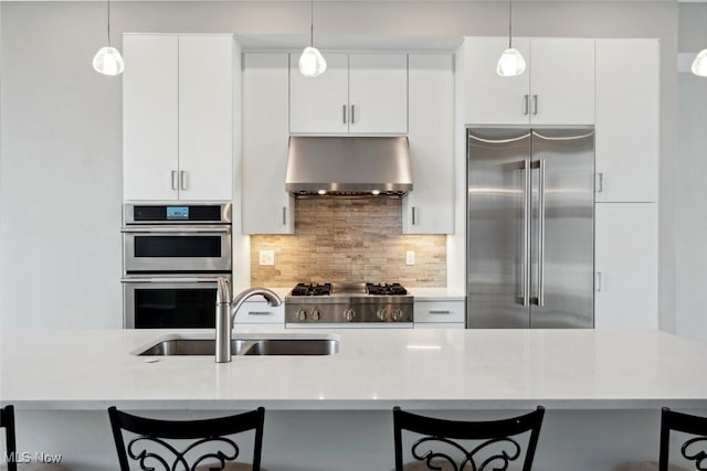 kitchen with appliances with stainless steel finishes, a sink, under cabinet range hood, a kitchen bar, and backsplash