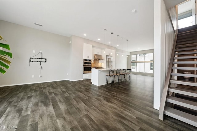 unfurnished living room featuring recessed lighting, dark wood-type flooring, visible vents, baseboards, and stairway