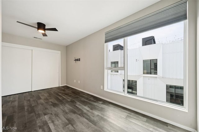 unfurnished bedroom with dark wood-style flooring, a closet, visible vents, a ceiling fan, and baseboards