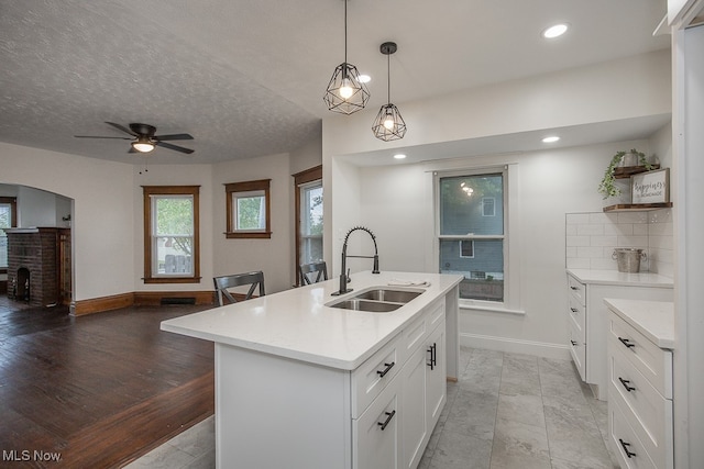 kitchen featuring an island with sink, hanging light fixtures, light hardwood / wood-style flooring, sink, and white cabinetry