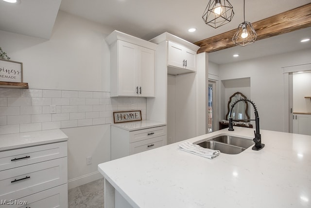 kitchen with white cabinets, hanging light fixtures, backsplash, light stone countertops, and sink