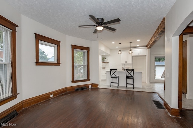 unfurnished living room featuring a textured ceiling, beamed ceiling, dark wood-type flooring, and ceiling fan