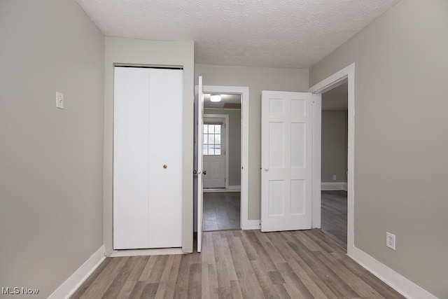 unfurnished bedroom featuring a closet, a textured ceiling, and light wood-type flooring