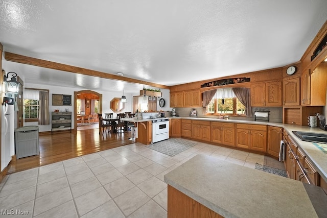 kitchen with kitchen peninsula, light tile patterned floors, a textured ceiling, sink, and white range