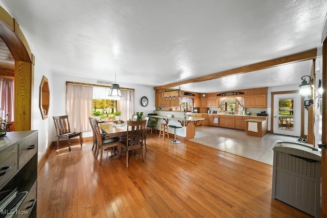 dining space with beam ceiling, a textured ceiling, and light hardwood / wood-style floors