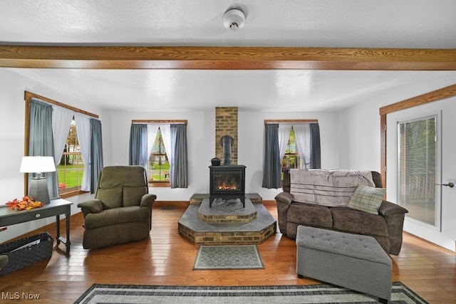 living room with hardwood / wood-style flooring, a wood stove, a wealth of natural light, and beam ceiling