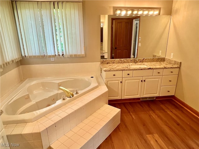 bathroom with hardwood / wood-style flooring, vanity, and a relaxing tiled tub