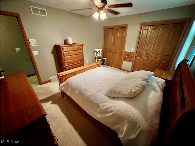 bedroom with light colored carpet, ceiling fan, and multiple closets