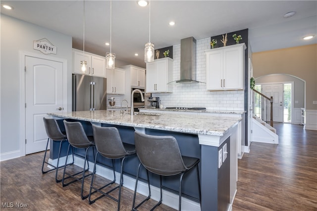 kitchen with white cabinetry, wall chimney exhaust hood, appliances with stainless steel finishes, and a kitchen island with sink