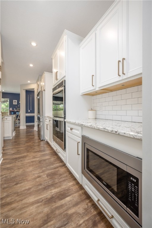 kitchen featuring dark wood-type flooring, appliances with stainless steel finishes, decorative backsplash, and white cabinetry