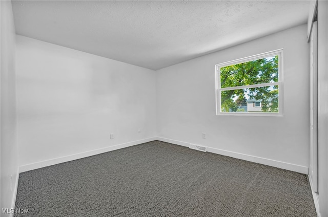 spare room with a textured ceiling and dark colored carpet