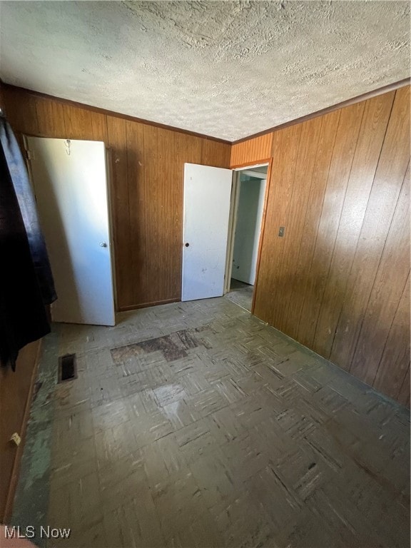 unfurnished room with a textured ceiling and wood walls