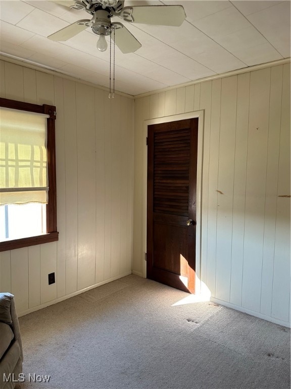 carpeted empty room with wooden walls and ceiling fan