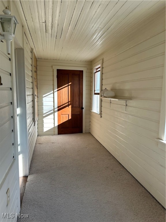 hall featuring wood walls, wooden ceiling, and carpet flooring