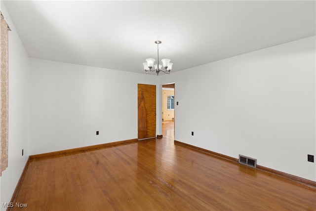 unfurnished room featuring an inviting chandelier and hardwood / wood-style floors