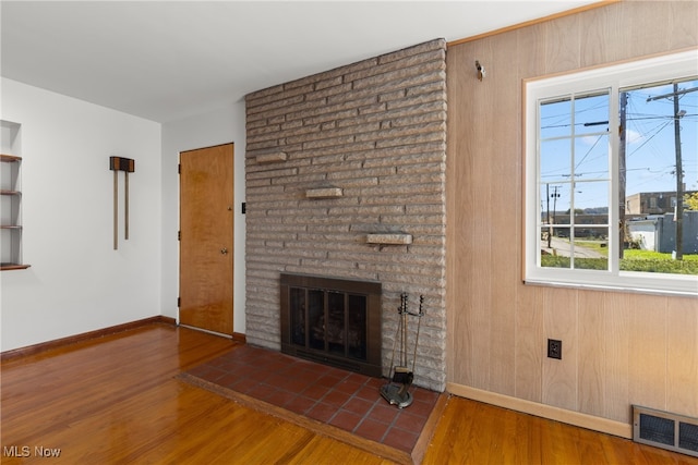 unfurnished living room featuring dark hardwood / wood-style floors, wooden walls, and a brick fireplace