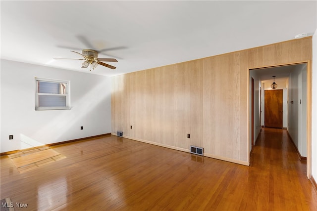 spare room with ceiling fan, hardwood / wood-style flooring, and wooden walls