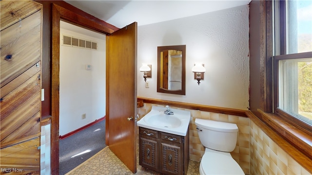 bathroom with vanity, toilet, tile walls, and a wealth of natural light