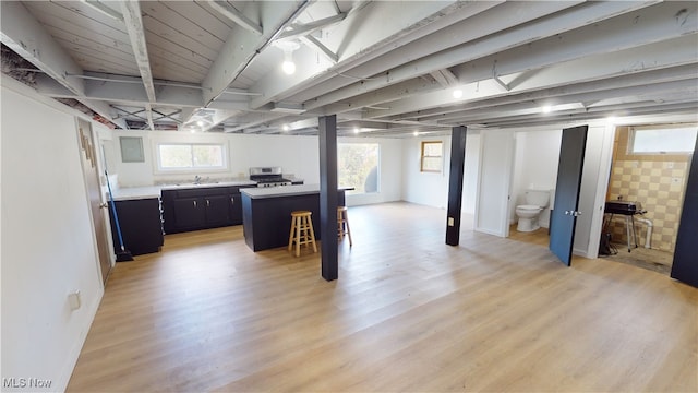 basement with sink, light wood-type flooring, and a healthy amount of sunlight