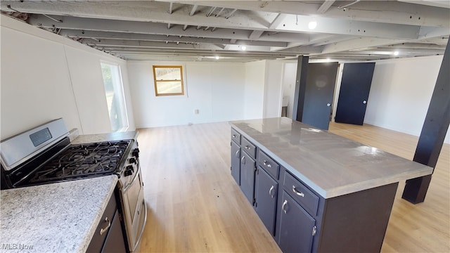 kitchen with stainless steel gas range oven, light hardwood / wood-style floors, light stone counters, and a kitchen island