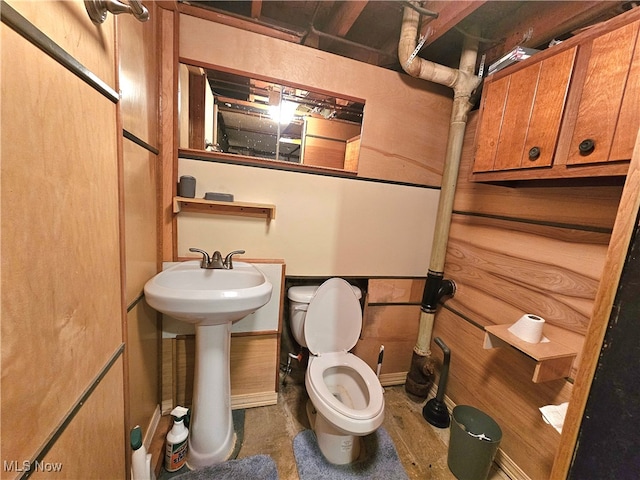 bathroom featuring toilet, sink, and wooden walls