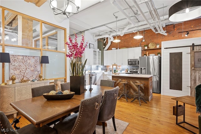 dining room featuring light hardwood / wood-style floors, a barn door, brick wall, and a high ceiling