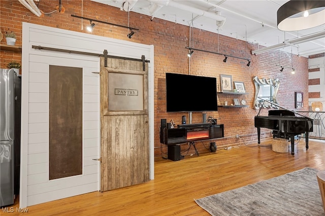 living room with brick wall, a high ceiling, a barn door, and hardwood / wood-style flooring