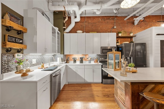 kitchen featuring decorative backsplash, white cabinets, appliances with stainless steel finishes, light wood-type flooring, and decorative light fixtures