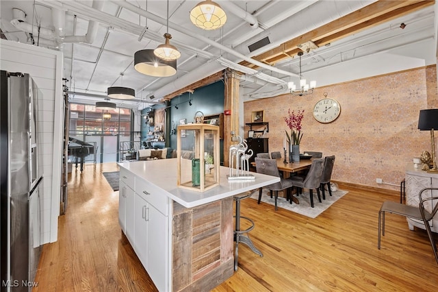 kitchen with light wood-type flooring, a kitchen island, decorative light fixtures, white cabinets, and stainless steel refrigerator