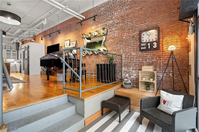 living room featuring brick wall, a towering ceiling, a fireplace, and hardwood / wood-style floors