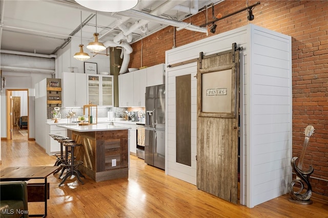 kitchen featuring a kitchen island, pendant lighting, white cabinets, brick wall, and light hardwood / wood-style flooring