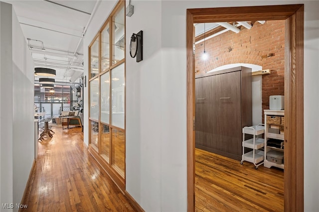 corridor featuring brick wall and wood-type flooring