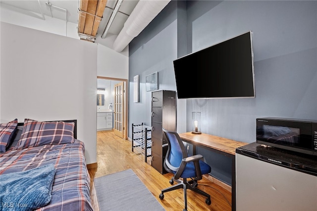 bedroom featuring refrigerator, a towering ceiling, ensuite bathroom, and light wood-type flooring