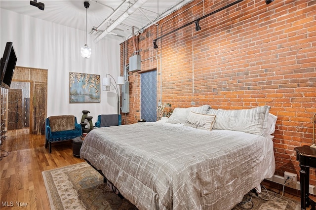 bedroom with light hardwood / wood-style flooring, brick wall, and a high ceiling