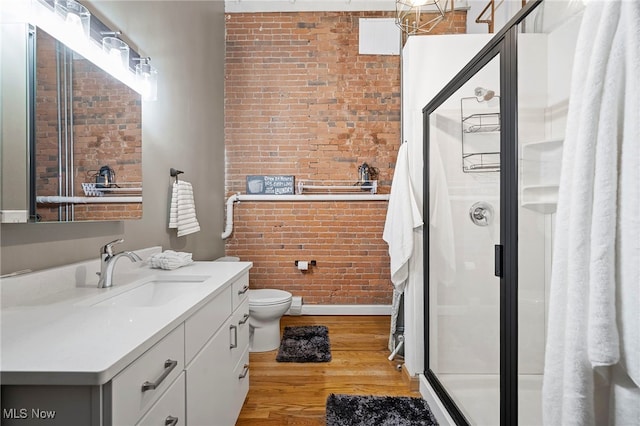 bathroom featuring wood-type flooring, an enclosed shower, toilet, vanity, and brick wall