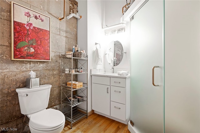 bathroom featuring toilet, a shower with shower door, vanity, hardwood / wood-style floors, and tile walls