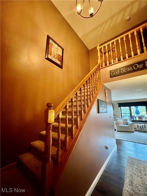 stairway with an inviting chandelier, lofted ceiling, and hardwood / wood-style flooring