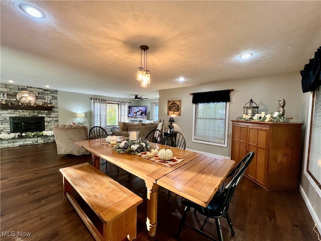 dining space featuring a stone fireplace, a textured ceiling, ceiling fan, and dark hardwood / wood-style floors