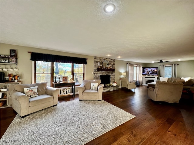 living room with a stone fireplace, dark hardwood / wood-style floors, a textured ceiling, and ceiling fan