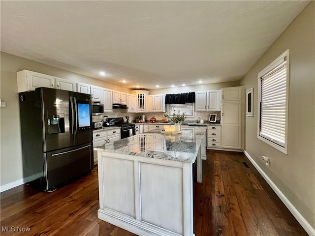 kitchen featuring appliances with stainless steel finishes, a center island, white cabinets, dark wood-type flooring, and light stone counters