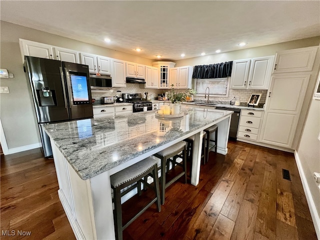 kitchen with appliances with stainless steel finishes, dark hardwood / wood-style flooring, a large island, white cabinets, and a breakfast bar area