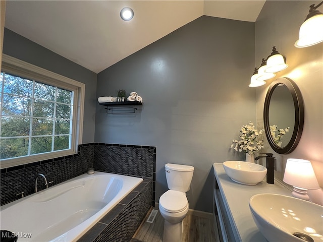 bathroom with a relaxing tiled tub, hardwood / wood-style floors, toilet, lofted ceiling, and vanity