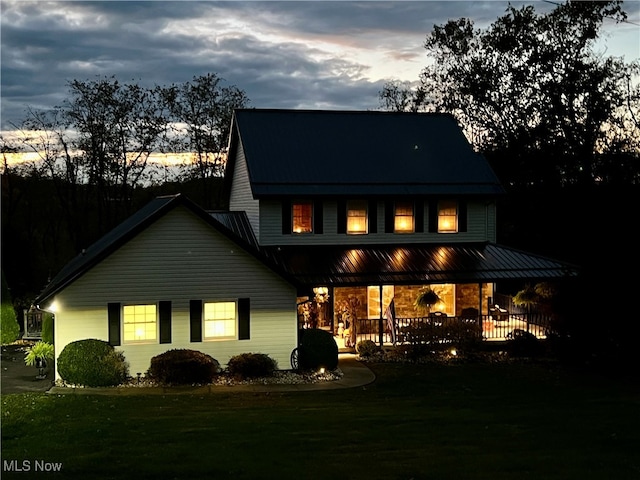 back house at dusk with a lawn and a porch