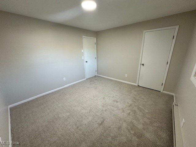 unfurnished bedroom with baseboard heating, light colored carpet, and a closet