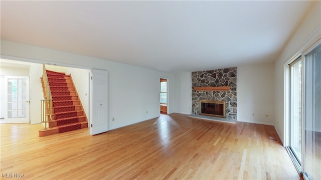 unfurnished living room with a stone fireplace and light wood-type flooring