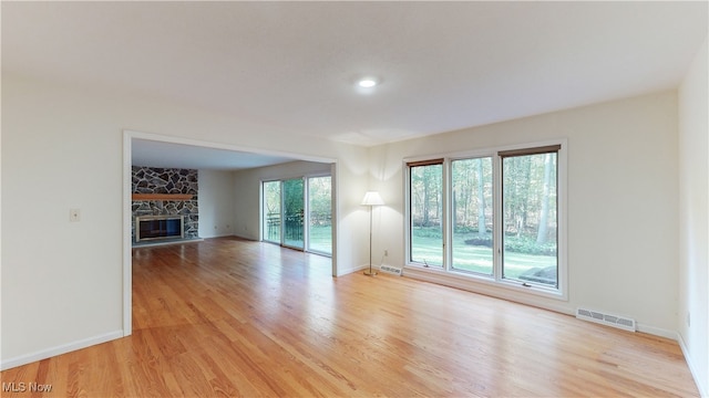 unfurnished living room featuring a stone fireplace and light wood-type flooring